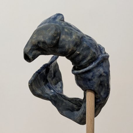Blau-graue Skulptur in Form eines geschwungenen, geometrischen Objekts auf einem Stock.